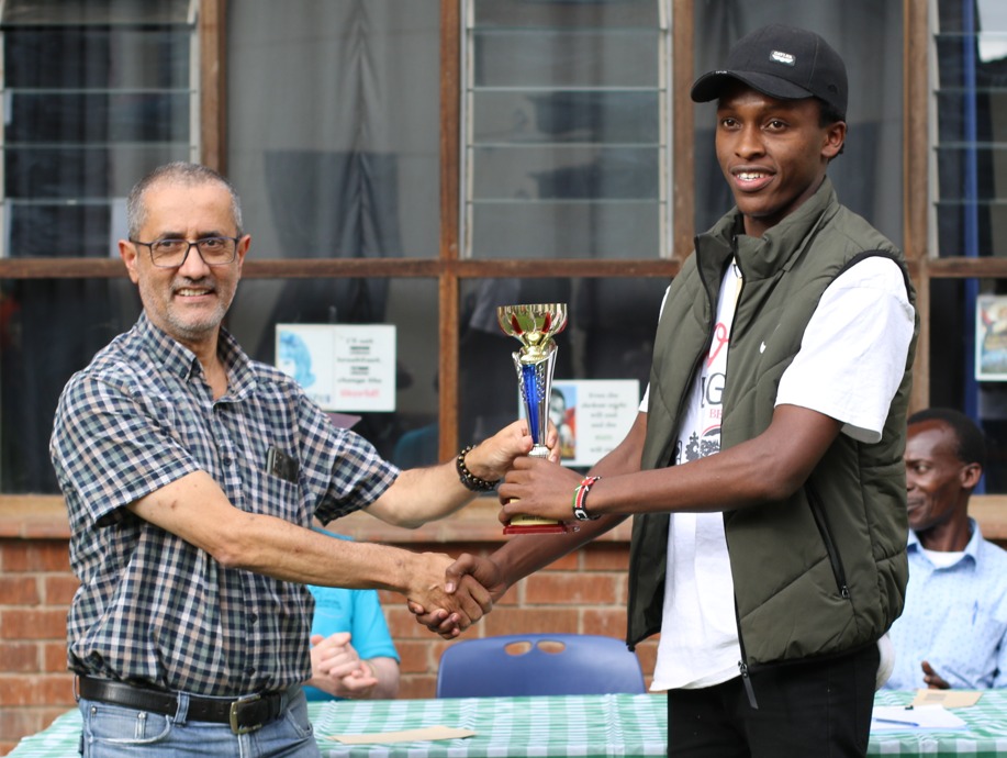 Kim Bhari (left) the tournament director presents Zaddock Nyakundi his trophy for winning the U1600 Section with a perfect score of 6/6.