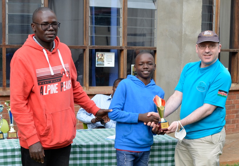 Warren Pollock (far right) the Nairobi Chess Club Secretary presents Jadon Simiyu his prize for the U1400 Section while his proud dad Jimmy looks on.